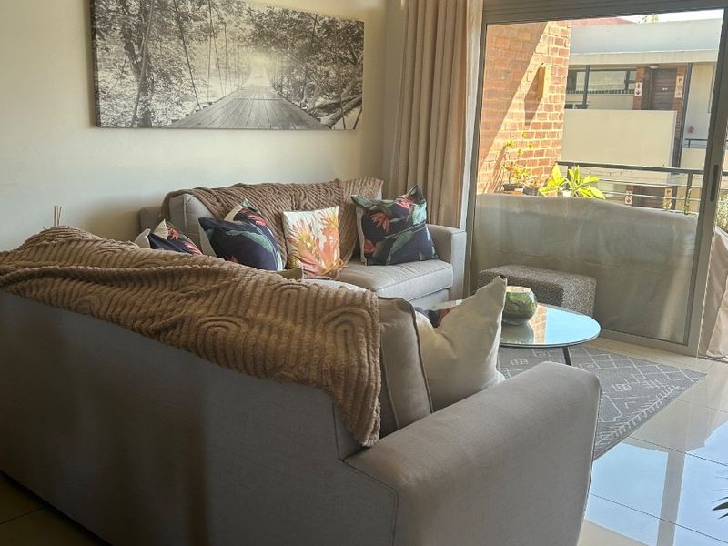A bright living room featuring large sliding glass doors that open onto a balcony, complemented by neutral tiled flooring.