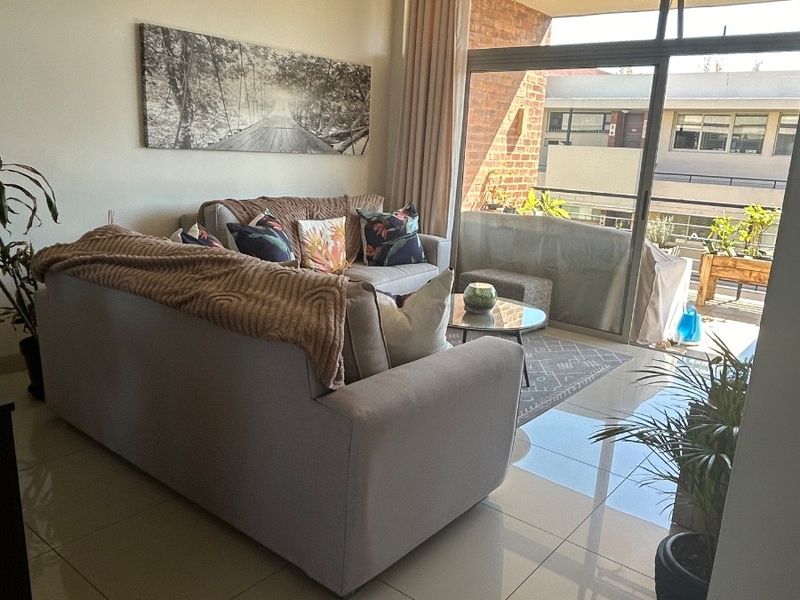 Bright living room featuring large sliding glass doors that open onto a private balcony, complemented by modern tiled flooring.