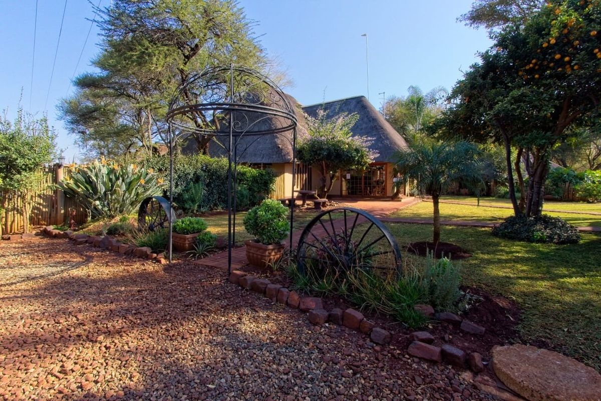 A well-maintained rear garden featuring a thatched roof dwelling, established trees, and a brick pathway leading to the home.
