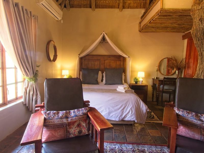 A rustic bedroom featuring a thatched ceiling, exposed timber elements, tiled flooring, and a split-system air conditioner.