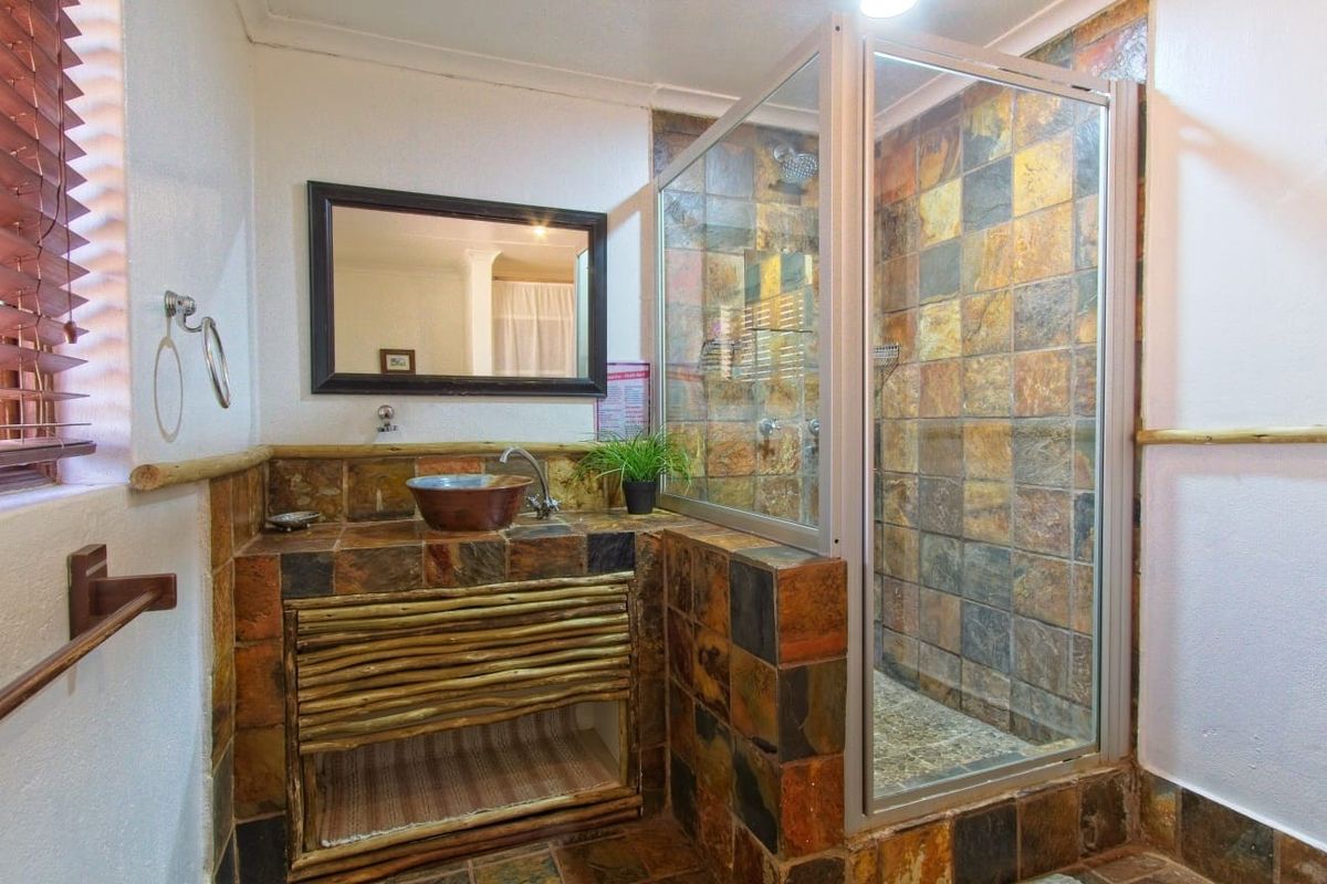 A rustic-style bathroom featuring a tiled shower enclosure, a custom vanity with a vessel sink, and natural stone tile finishes.