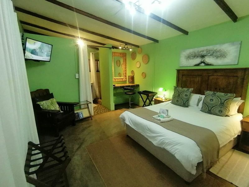 A bedroom featuring exposed timber ceiling beams, a built-in vanity area, and an en-suite bathroom, finished with vibrant green walls.