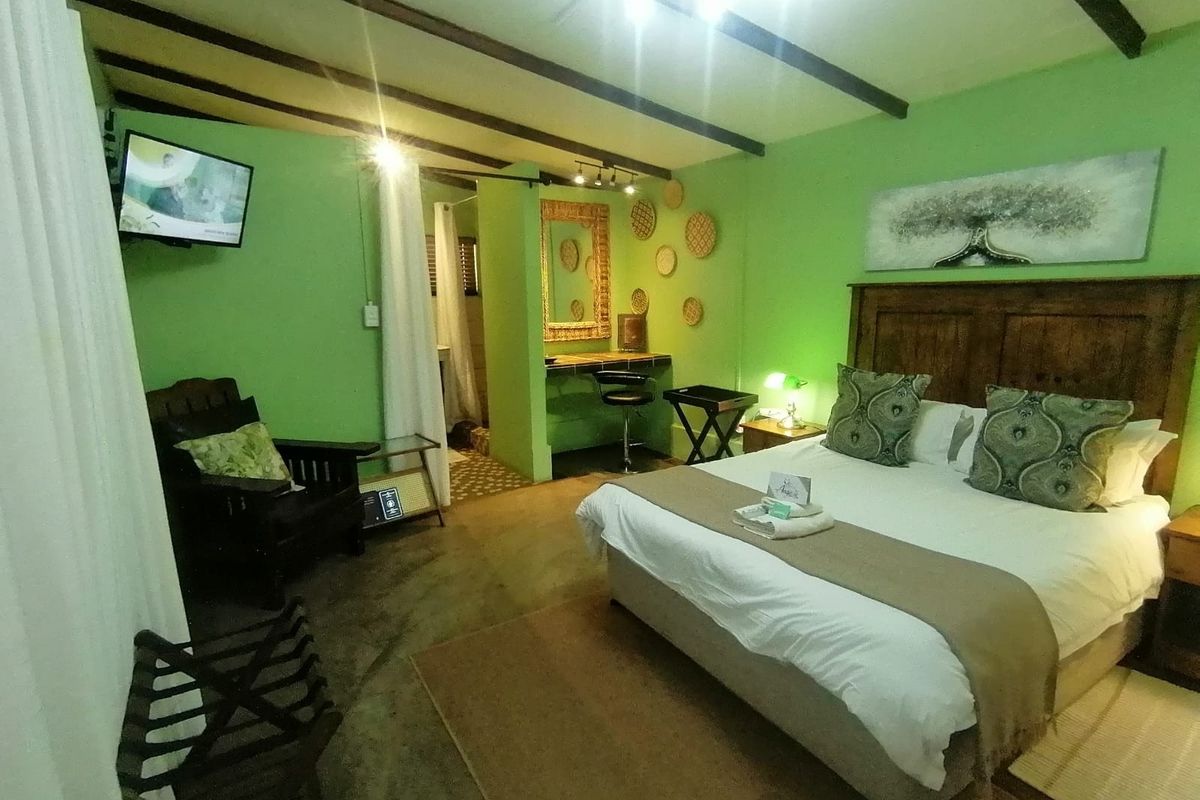 A bedroom featuring exposed timber ceiling beams, a built-in vanity area, and an en-suite bathroom, finished with vibrant green walls.