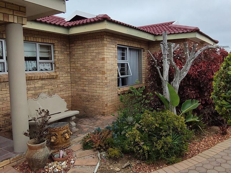 A front exterior view of a face brick house featuring a tiled roof, aluminium window frames, and a paved entrance area with established garden landscaping.