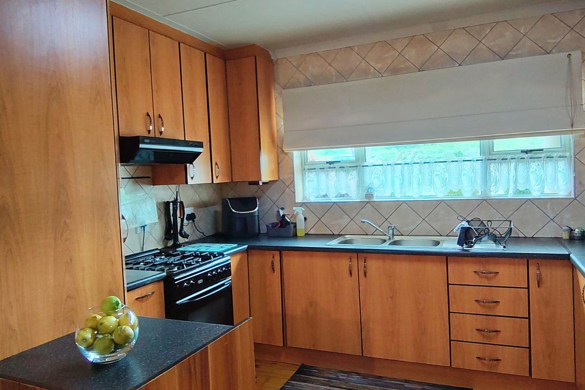 A functional kitchen featuring wood-look laminate cabinetry, dark countertops, a gas stove with extractor fan, and a double bowl sink under a window.