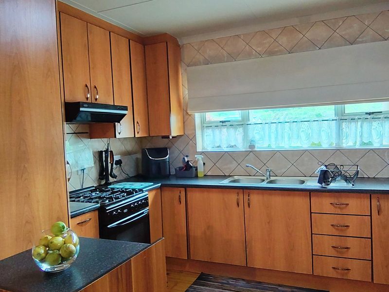 A functional kitchen featuring wood-look laminate cabinetry, dark countertops, a gas stove with extractor fan, and a double bowl sink under a window.