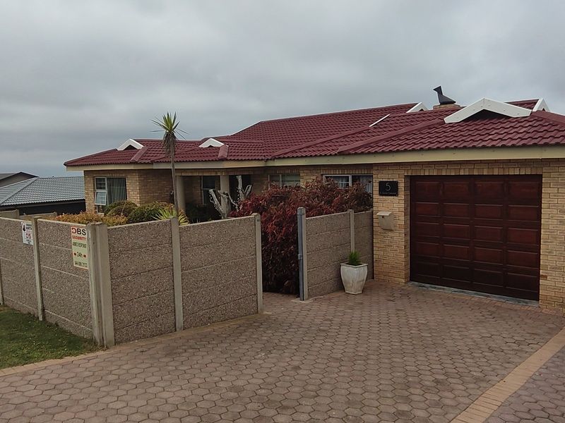 Front view of a single-story brick house featuring a tiled roof, paved driveway, and a secure precast concrete boundary wall.