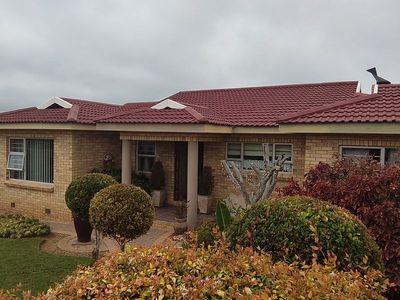 A well-maintained single-story face brick house featuring a red tiled roof, a covered entrance porch with concrete columns, and a paved front walkway.