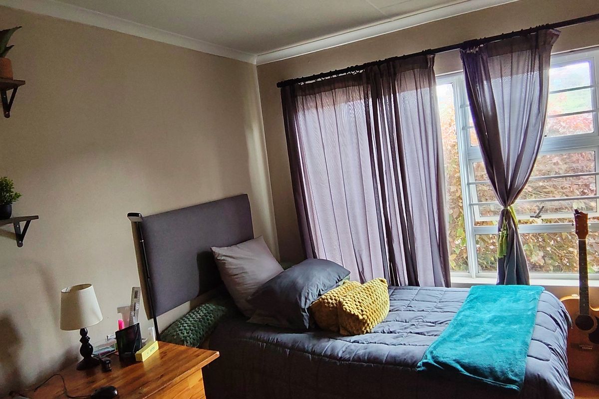 A cozy bedroom featuring a window with curtains and neutral wall tones, providing a comfortable and functional sleeping space.