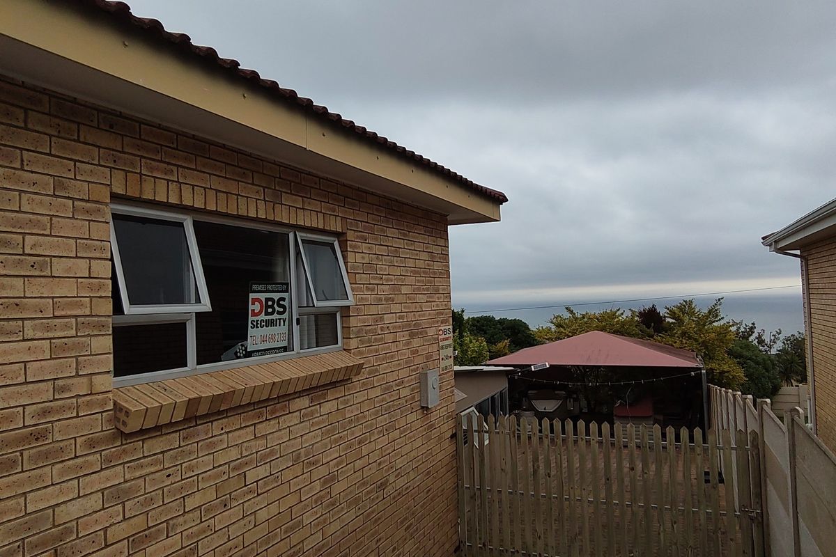 Rear exterior view of the property featuring face brick walls, aluminium windows, and a fenced outdoor area with a covered patio.