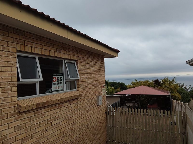 Rear exterior view of the property featuring face brick walls, aluminium windows, and a fenced outdoor area with a covered patio.