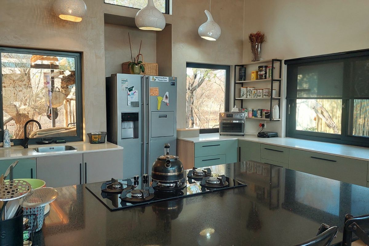 Modern kitchen featuring sleek cabinetry, stone countertops, a central island with a built-in gas hob, and large windows providing natural light and garden views.