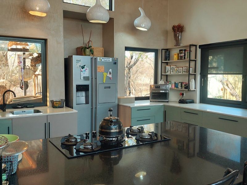 Modern kitchen featuring sleek cabinetry, stone countertops, a central island with a built-in gas hob, and large windows providing natural light and garden views.