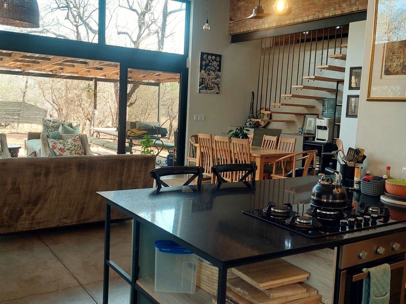 Spacious open-plan living area featuring a modern kitchen island with gas hob, exposed brick accents, floating staircase, and large sliding doors to the patio.