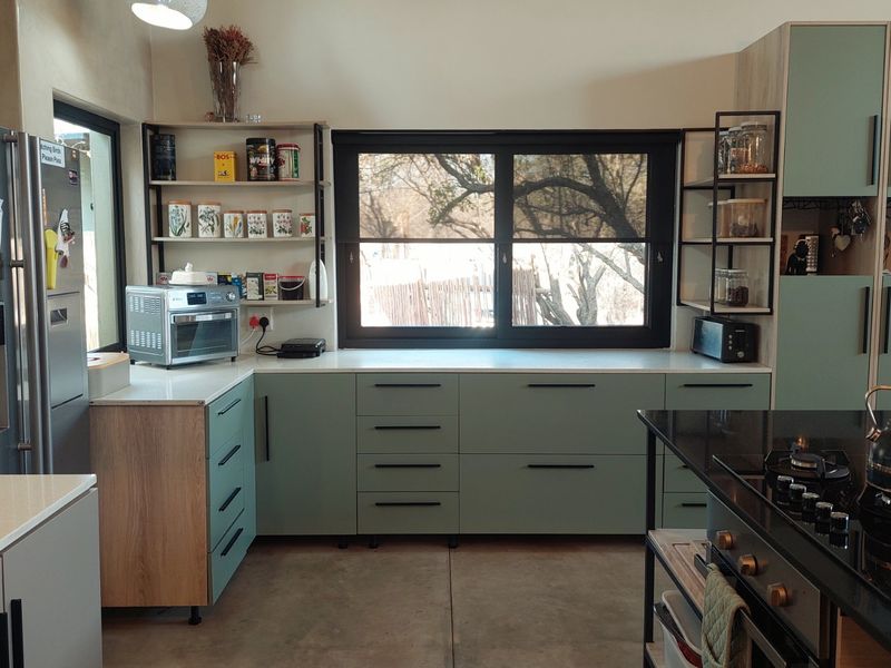 Modern kitchen featuring sage green cabinetry, stone countertops, a central island with a gas hob, and polished concrete flooring.