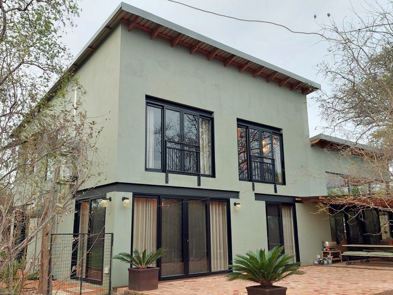 A modern two-story home featuring a light green stucco facade, black aluminum window and door frames, and a spacious brick-paved rear patio area.