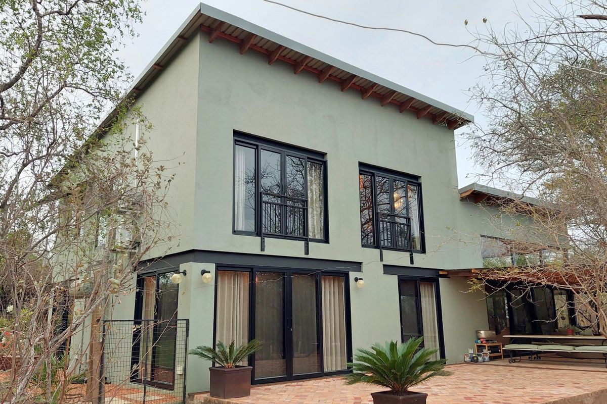 A modern two-story home featuring a light green stucco facade, black aluminum window and door frames, and a spacious brick-paved rear patio area.