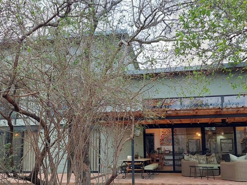Rear view of the property featuring a spacious paved patio area covered by a timber pergola, with large sliding glass doors leading indoors.