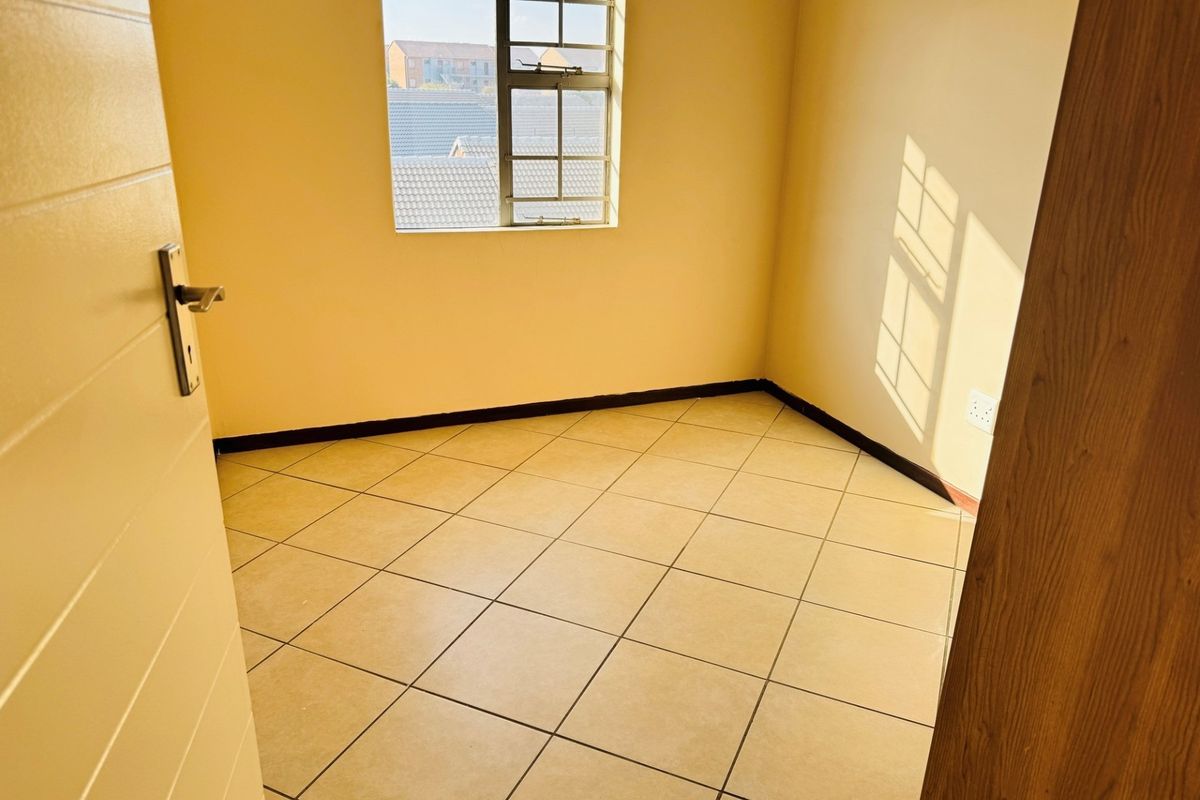 A bright, empty bedroom featuring neutral tiled flooring, clean walls, and a window with security bars, offering a blank canvas for personalization.