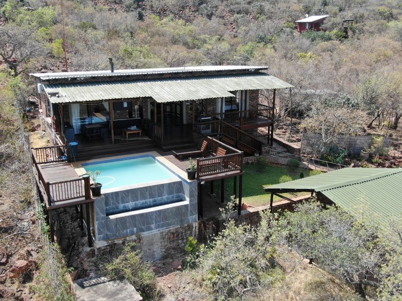 Aerial view of a rustic small holding featuring a raised timber deck, swimming pool, and corrugated metal roofing set in a natural landscape.