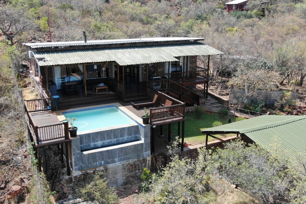 Aerial view of a rustic small holding featuring a raised timber deck, swimming pool, and corrugated metal roofing set in a natural landscape.