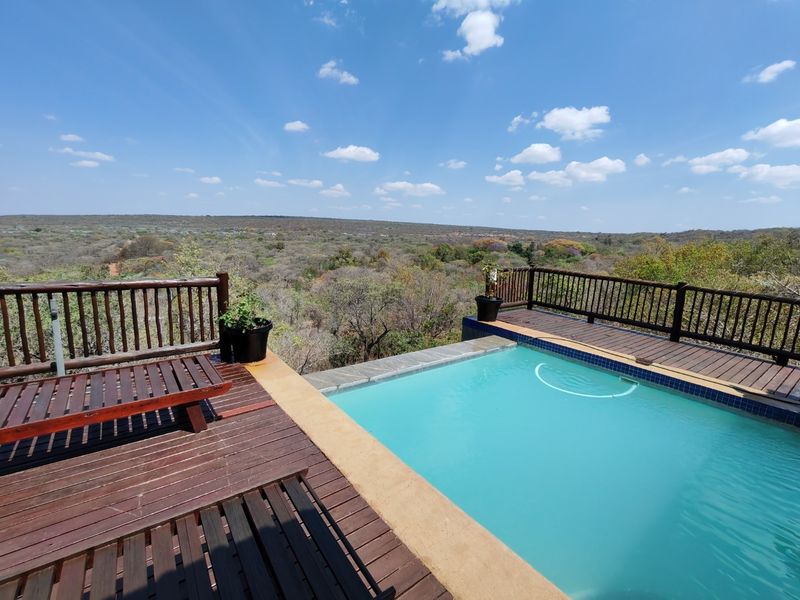 An elevated swimming pool area featuring wooden decking and a balustrade, offering expansive views over the surrounding natural landscape.
