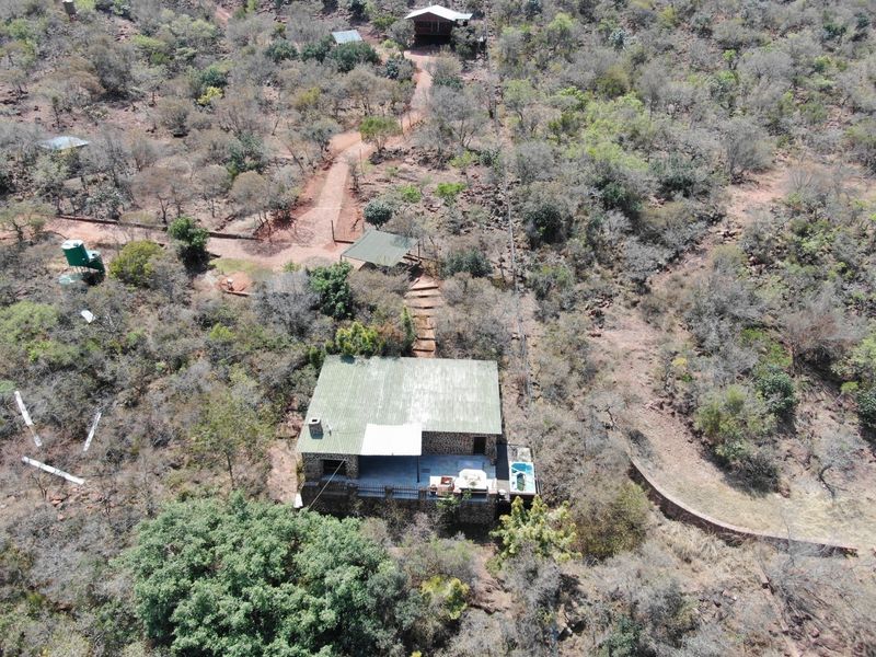 Aerial view of a rural small holding featuring a stone-walled dwelling with a metal roof, outdoor patio, plunge pool, and surrounding natural bushveld landscape.