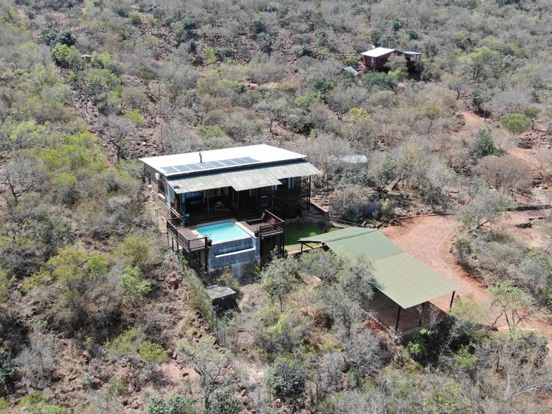 Aerial view of a small holding property featuring a main dwelling with solar panels, a swimming pool, wooden decking, and a separate carport structure.