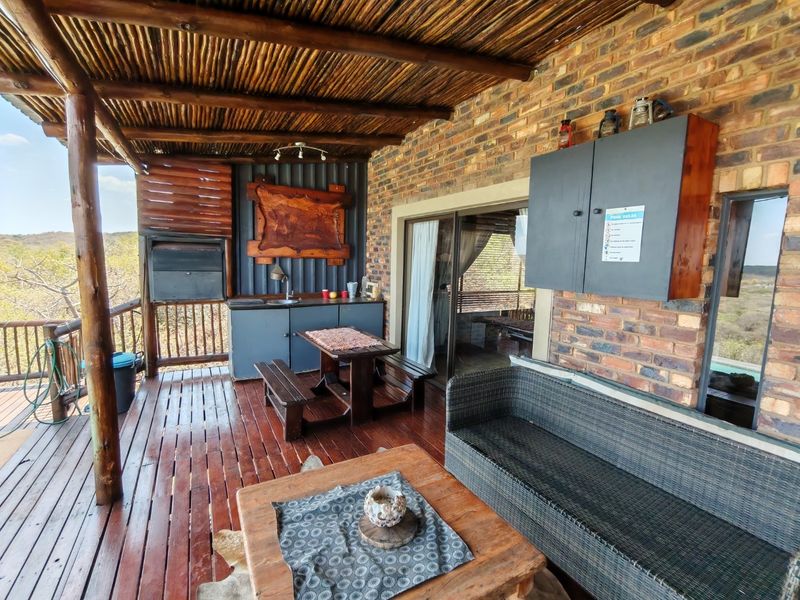 Covered outdoor patio featuring a wooden deck, built-in braai, and a small prep area with a sink, overlooking the surrounding landscape.