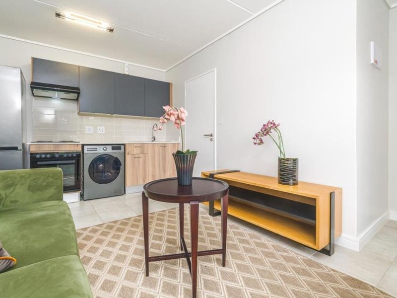 An open-plan living area featuring a compact kitchen with modern cabinetry, built-in oven, hob, extractor fan, and tiled flooring throughout.
