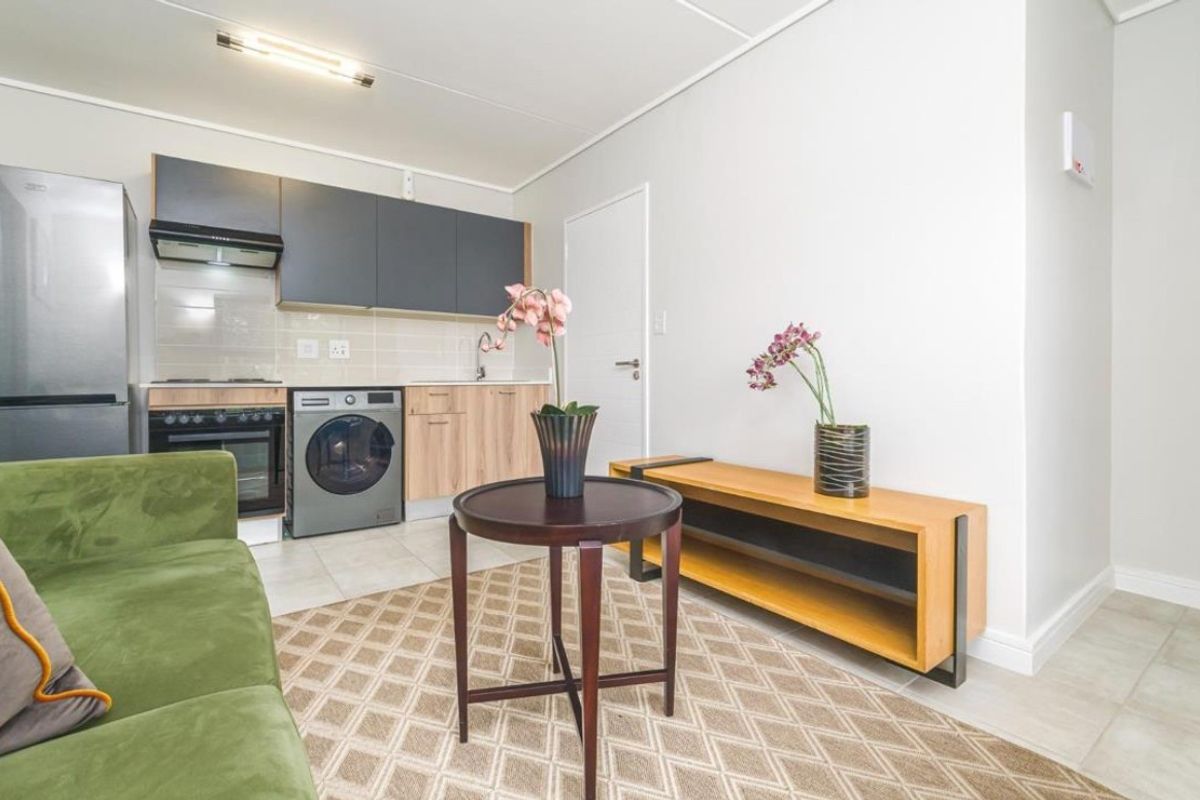 An open-plan living area featuring a compact kitchen with modern cabinetry, built-in oven, hob, extractor fan, and tiled flooring throughout.