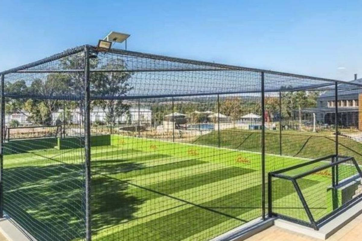 A well-maintained outdoor sports facility featuring an enclosed artificial turf court with goal posts and integrated floodlighting.
