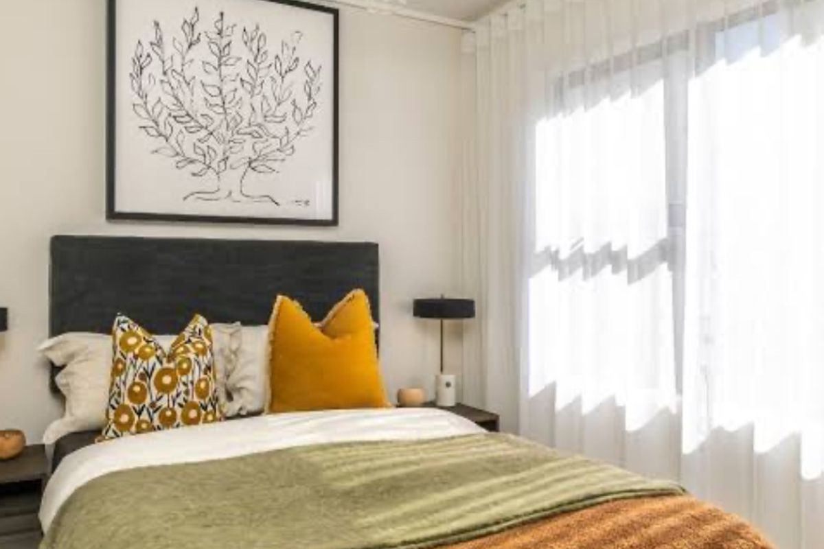 A well-lit bedroom featuring neutral walls, a pendant light fixture, and floor-to-ceiling curtain tracks.