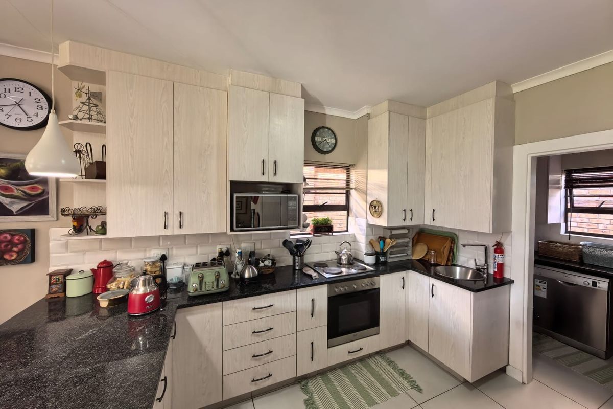A functional kitchen featuring light wood-grain cabinetry, granite countertops, subway tile backsplash, and integrated appliances, with an adjacent scullery area.