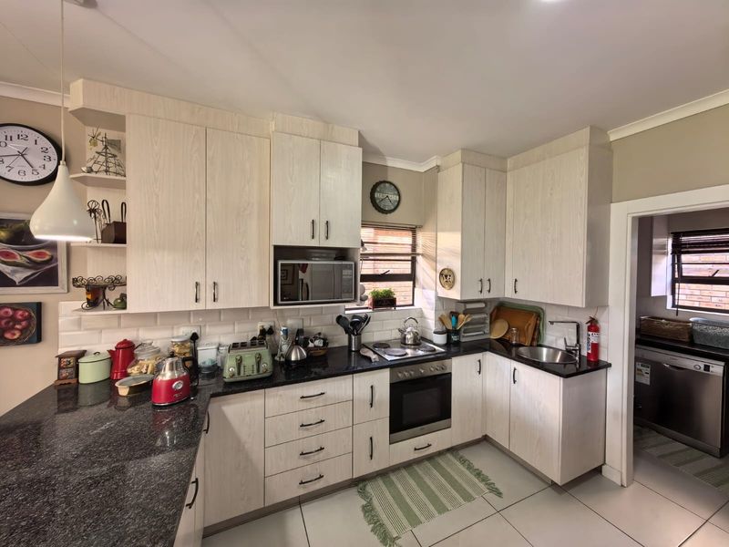 A functional kitchen featuring light wood-grain cabinetry, granite countertops, subway tile backsplash, and integrated appliances, with an adjacent scullery area.