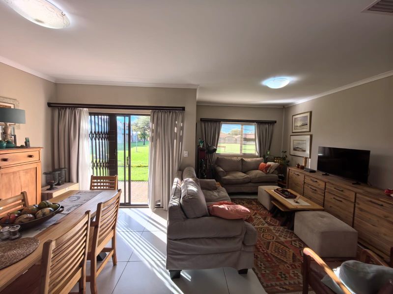 Spacious open-plan living and dining area featuring tiled flooring, large sliding doors with security gate, and natural light, leading to an outdoor garden space.