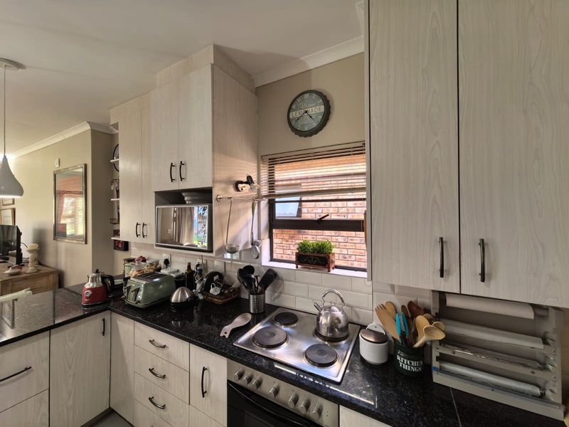 A functional kitchen featuring light wood-grain cabinetry, dark granite countertops, a built-in electric hob and oven, and a classic subway tile backsplash.