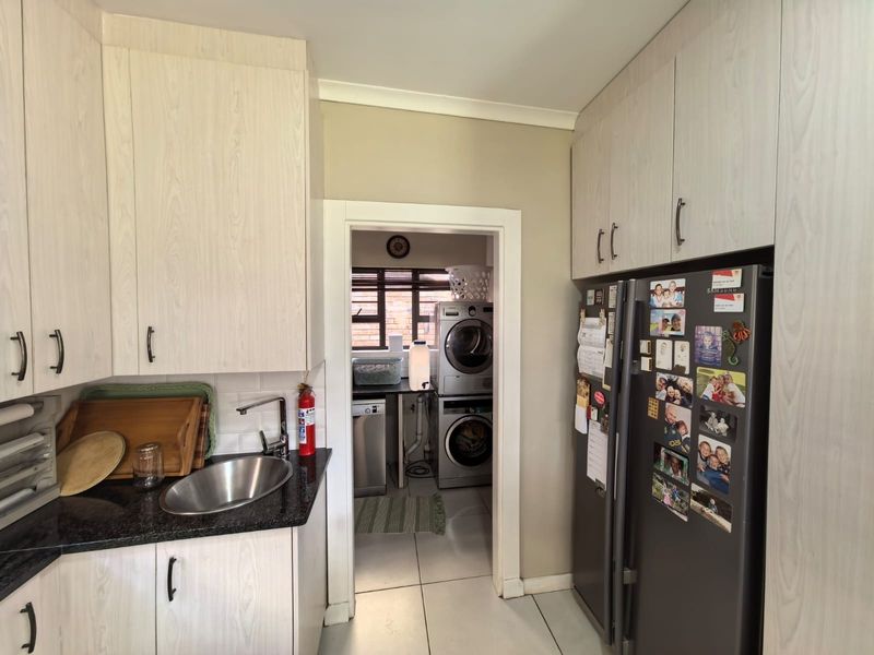 A functional scullery and laundry area featuring built-in cabinetry, a stainless steel sink, and dedicated space for laundry appliances.