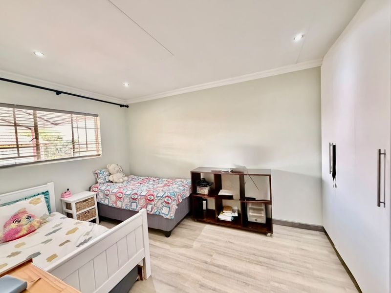 A well-lit bedroom featuring light-toned laminate flooring, built-in cupboards, and recessed ceiling lighting, providing a clean and functional living space.