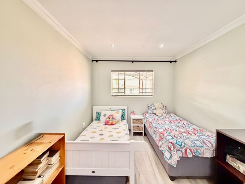 A well-lit bedroom featuring laminate flooring, recessed downlighting, and a window with fitted blinds, providing a clean and functional living space.
