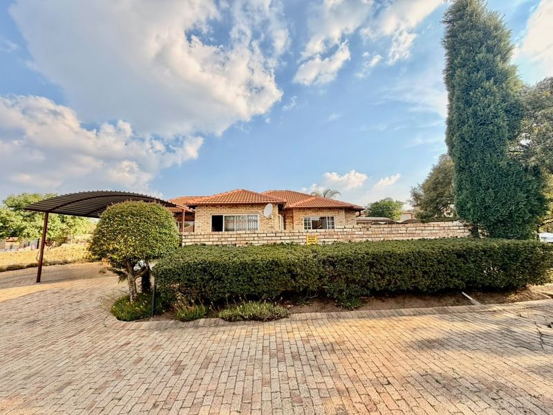 Front view of a brick house featuring a tiled roof, a paved driveway, and a covered carport area.
