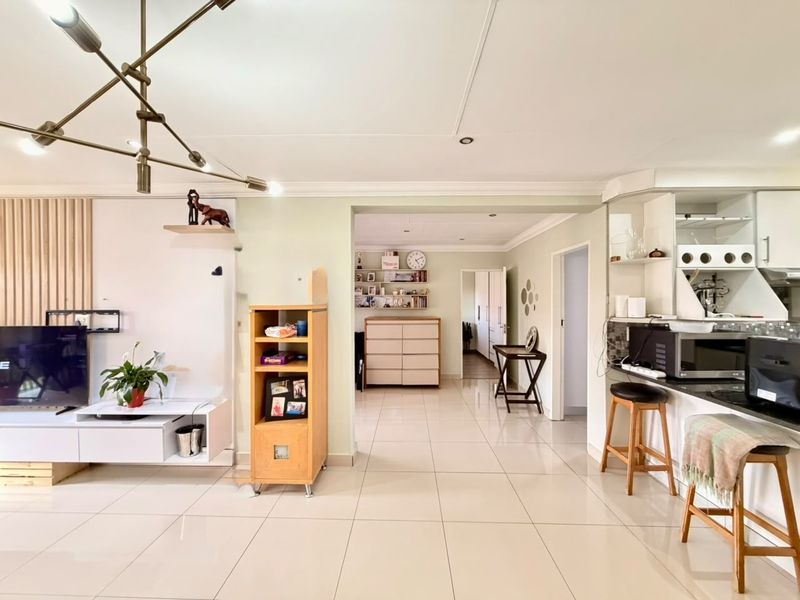 Spacious open-plan living area featuring tiled floors, modern kitchen cabinetry with granite countertops, and a decorative feature wall.
