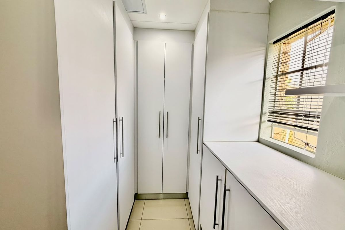A clean and modern walk-in closet or dressing area featuring ample built-in white cabinetry, tiled flooring, and natural light from a side window.
