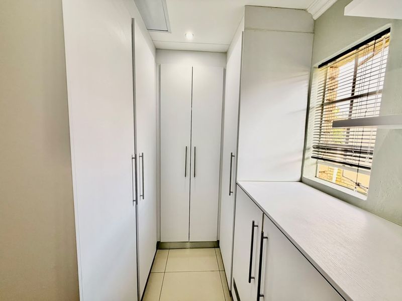 A clean and modern walk-in closet or dressing area featuring ample built-in white cabinetry, tiled flooring, and natural light from a side window.