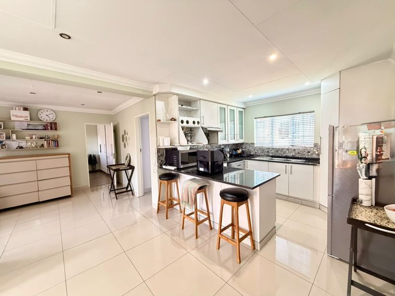 Open plan kitchen featuring white cabinetry, granite countertops, a central island, and tiled flooring, seamlessly connecting to the adjacent living area.