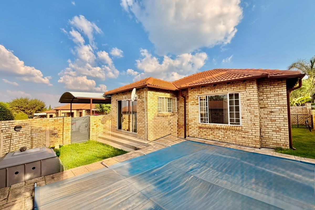 Rear view of a brick house featuring a swimming pool with a cover, a paved patio area, and an attached carport.