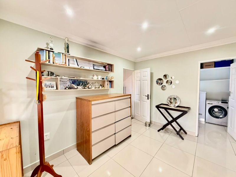 A bright, well-maintained hallway featuring neutral tiled flooring, recessed downlighting, and built-in wall shelving, with an adjacent laundry area visible.
