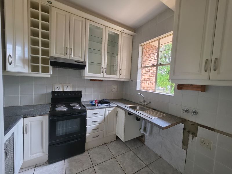A functional kitchen featuring white cabinetry, granite countertops, and a tiled splashback, currently requiring minor repairs to the cabinetry and plumbing area.