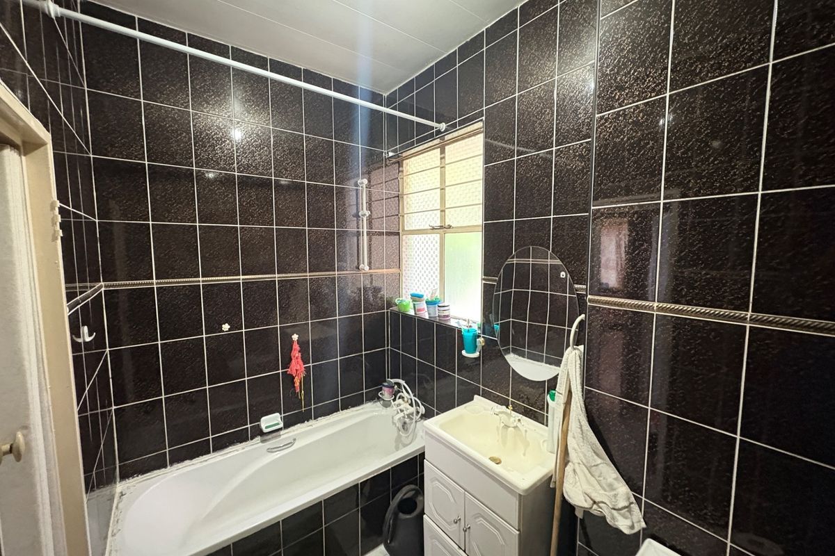 A compact bathroom featuring dark wall tiles, a built-in bathtub, and a vanity basin unit.