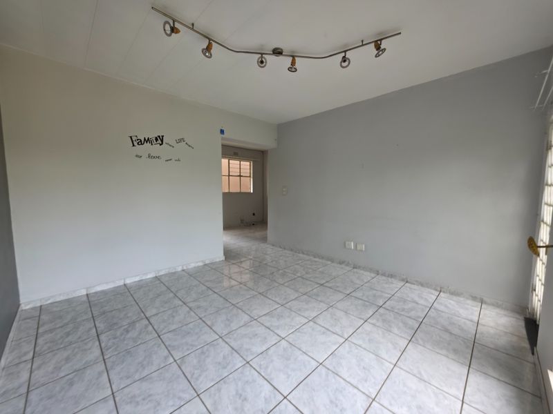 An empty living room featuring neutral tiled flooring, track lighting, and a security gate, offering a clean canvas for personalization.